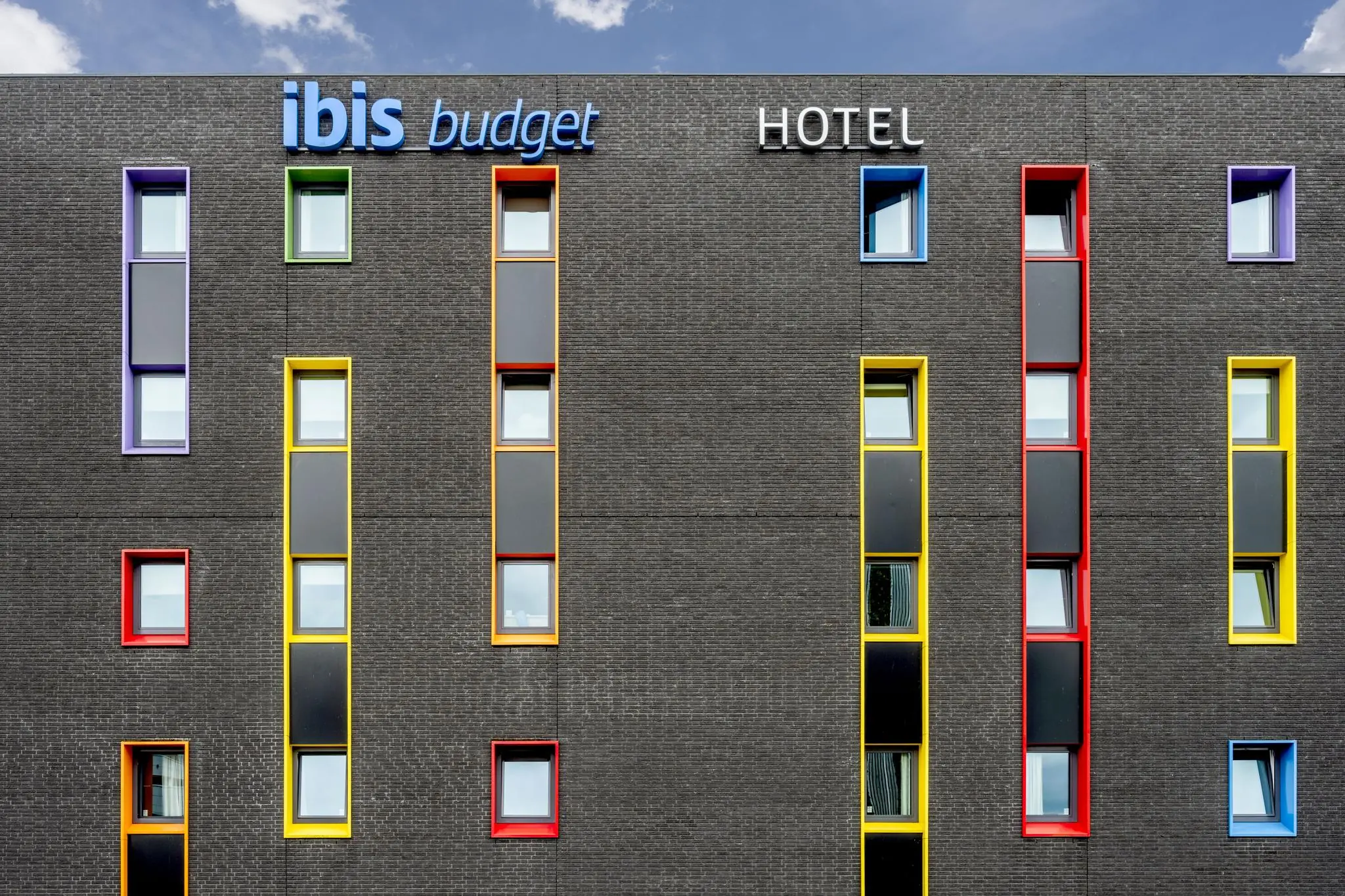 Voorgevel van het ibis budget Hotel aan het Airportplein in Rotterdam, met gekleurde raamomlijstingen tegen een donkere bakstenen muur.
